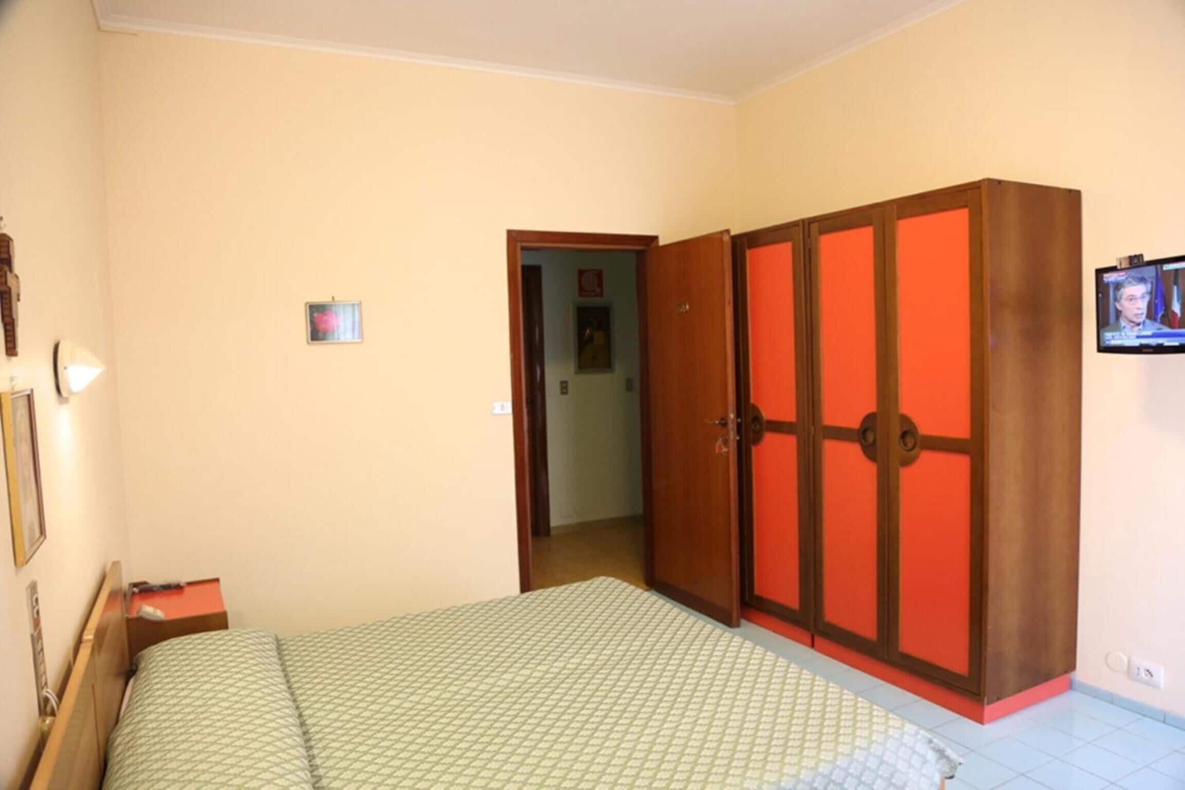 Een slaapkamer met een bed, een kledingkast, een televisie en een deur naar een andere kamer.