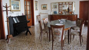 Un coin repas agrémenté d’un piano, d’une table ronde en verre et de chaises à motifs floraux.
