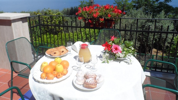 Une table de balcon dressée avec des éléments pour le petit-déjeuner, une vue sur une montagne et un plan d’eau.