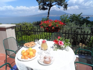 Une table de balcon dressée avec des éléments pour le petit-déjeuner, une vue sur une montagne et un plan d’eau.