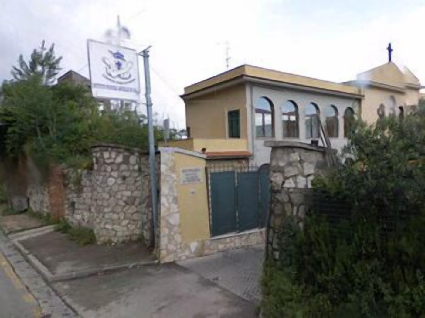 A building with a stone wall entrance, a small gate, and a sign with a crest.