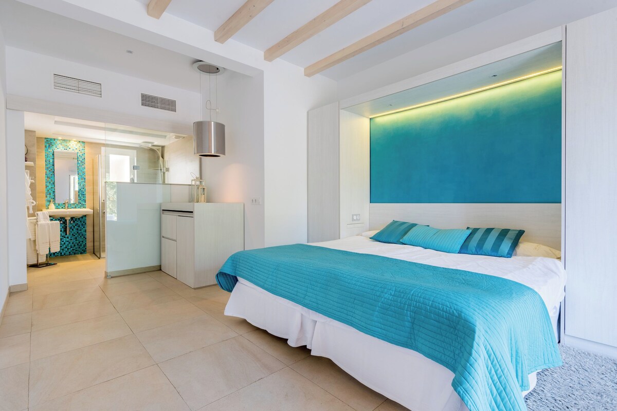 Ein modernes Schlafzimmer mit einem großen Bett, einer eingebauten Kopfteil und Blick auf den Himmel durch ein Fenster.