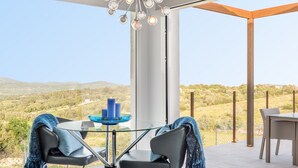 Ein moderner Außenbereich mit Tisch aus Glas, zwei Stühlen und Blick auf eine hügelige Landschaft.