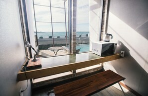 A kitchen with a view of a pool and ocean, a kettle on the microwave, and a wooden shelf. - Aqua BEAutique (Jeju City)