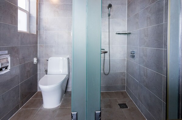 A modern bathroom with a toilet, shower, and glass partition. - Aqua BEAutique (Jeju City)