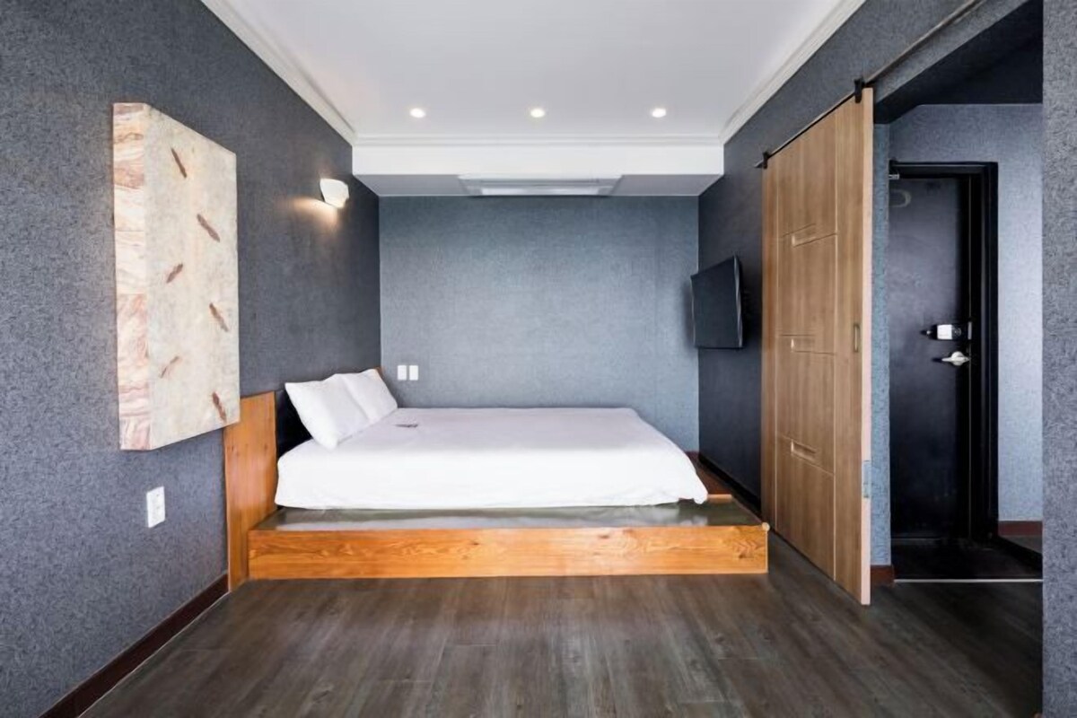 A modern bedroom with a wooden bed frame, a gray textured wall, and a sliding wooden door.