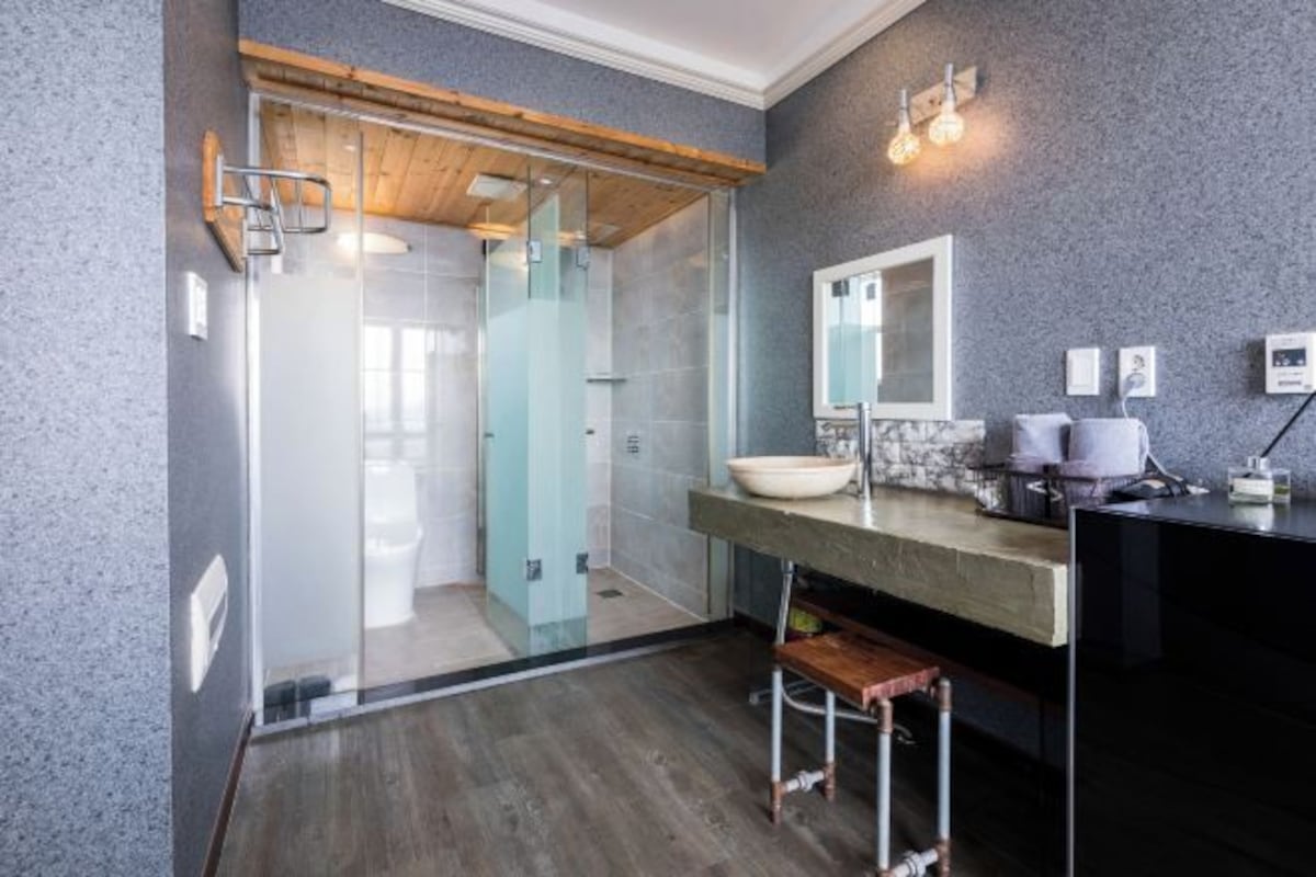 Un baño moderno con cabina de ducha de vidrio, techo de madera, lavabo de mármol y encimera negra.