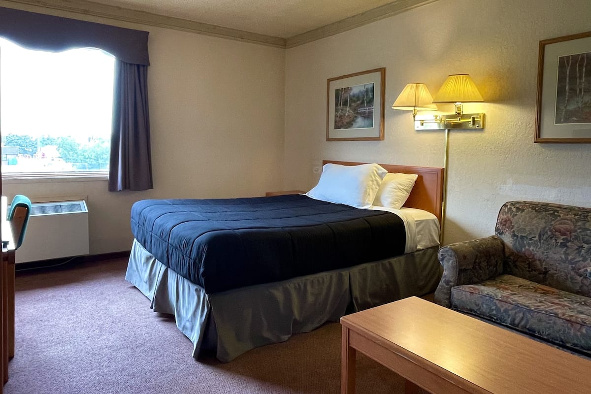Una habitación de hotel con cama, sofá, mesa y ventana con cortinas.