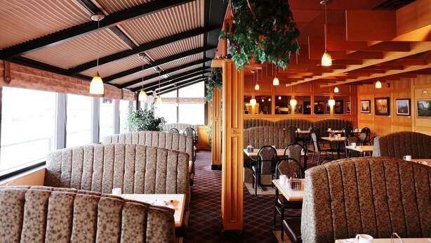 A restaurant with booth seating, hanging plants, and pendant lighting. - Tamarack Motor Inn (Rocky Mountain House)