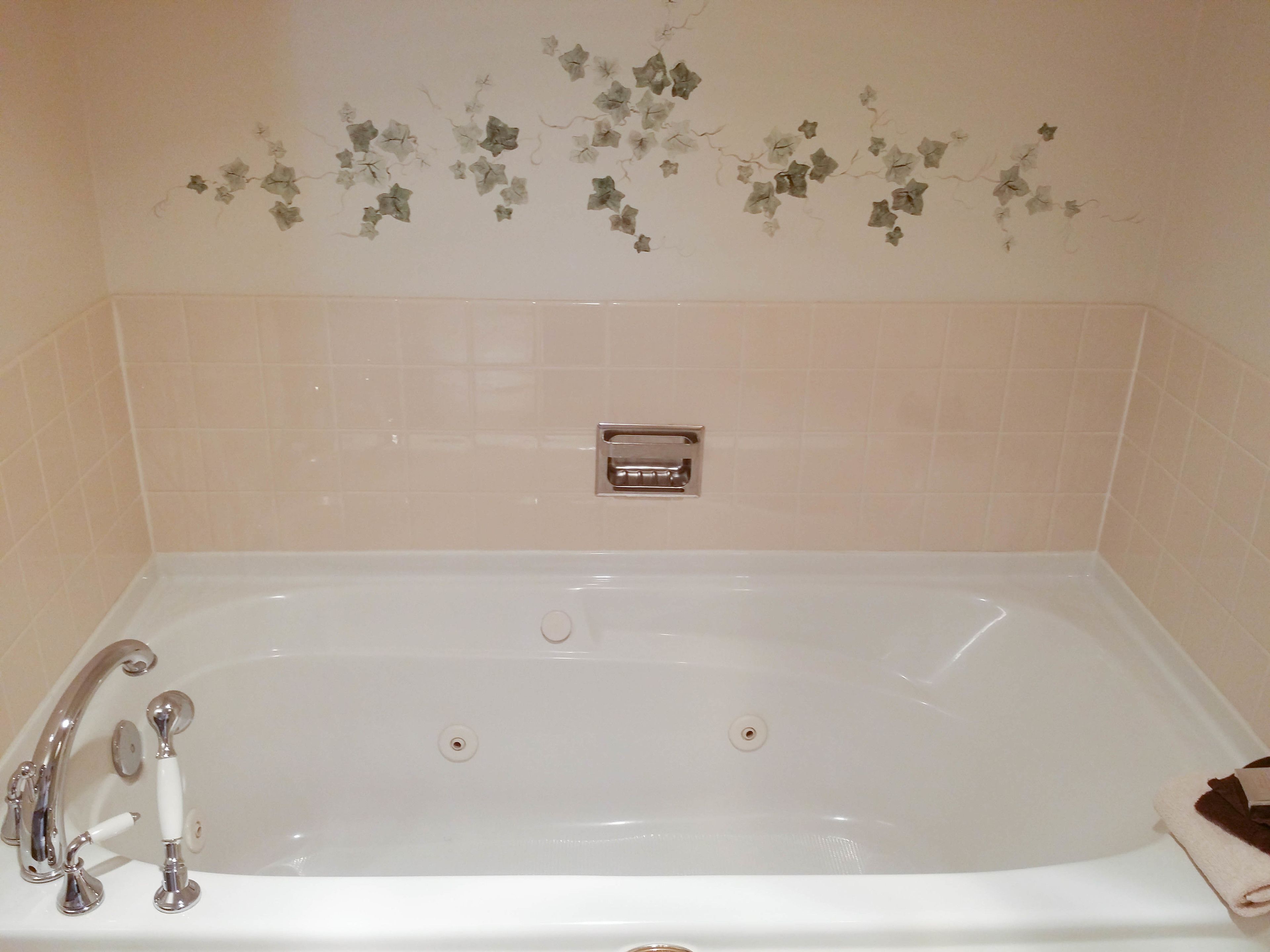 Una bañera blanca con accesorios cromados, una toalla al lado y azulejos decorativos en la pared.