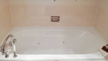 Una bañera blanca con accesorios cromados, una toalla al lado y azulejos decorativos en la pared.