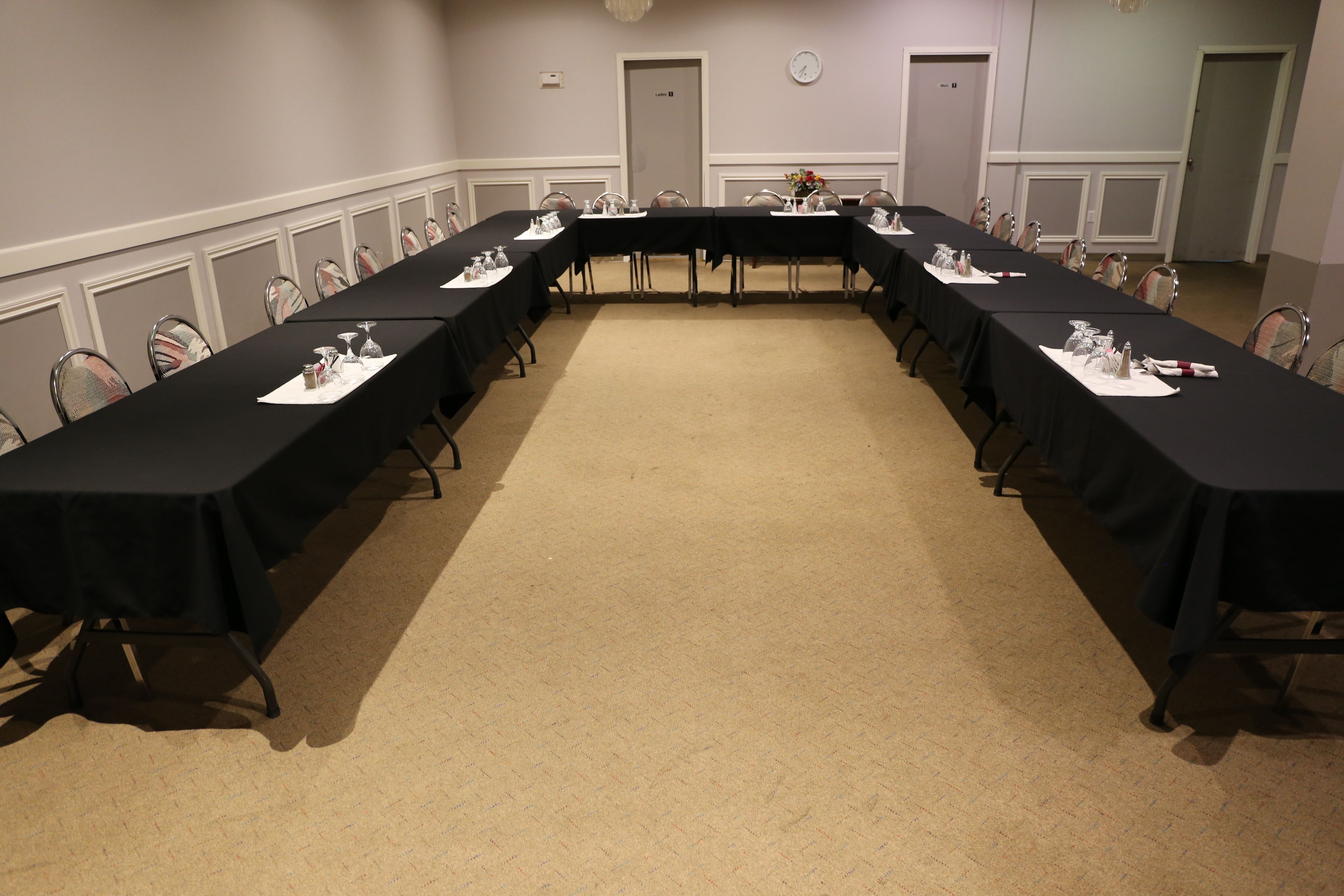 A conference room with long tables, chairs, and a carpeted floor.