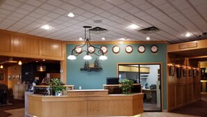 A reception area with a wooden reception desk, multiple clocks on the wall, and a chandelier. - Tamarack Motor Inn (Rocky Mountain House)