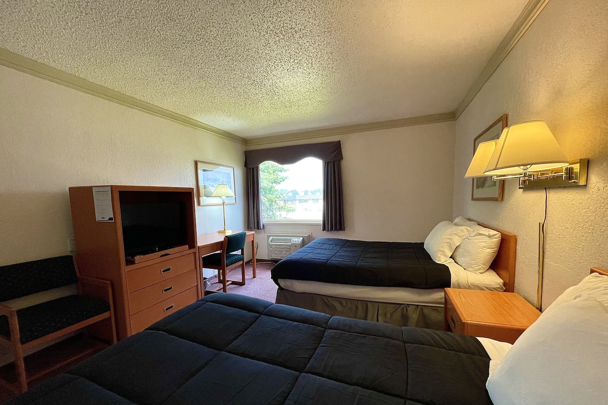 Habitación de hotel con dos camas, un escritorio, televisor y ventana con cortinas.
