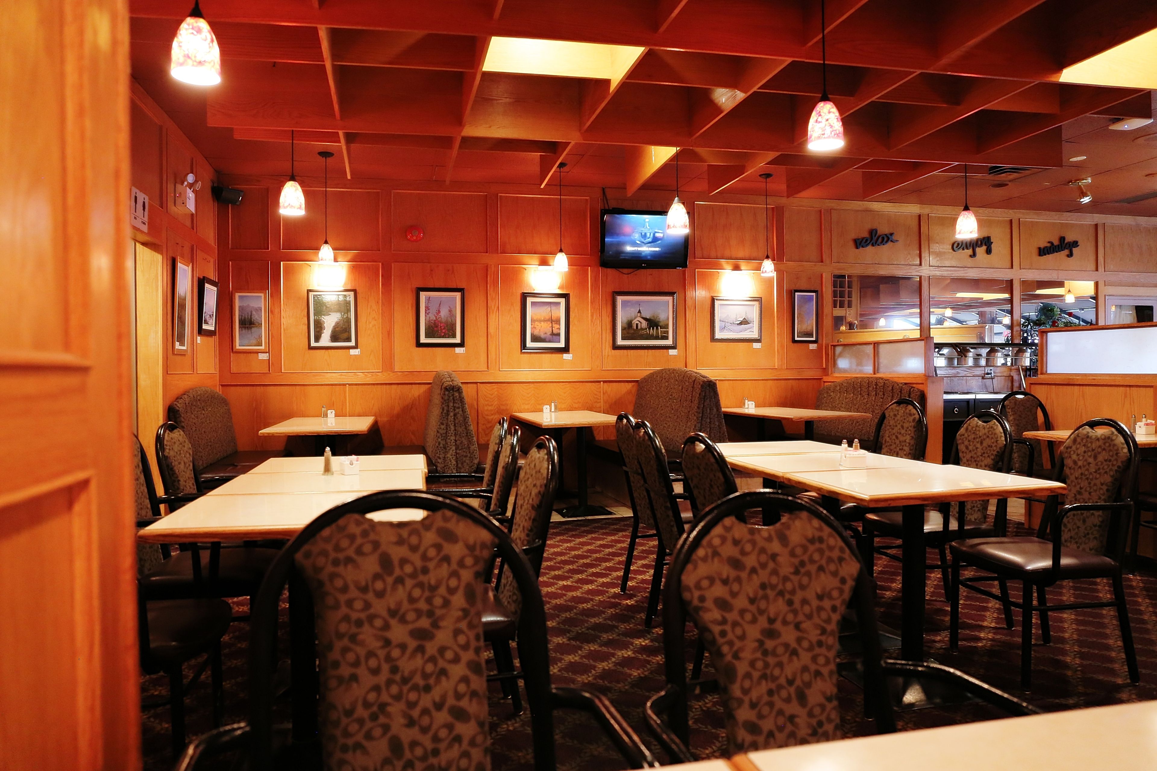 Un restaurant aux murs lambrissés, orné de tableaux encadrés, et dont les tables sont accompagnées de chaises.