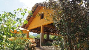 Una casa rústica amb una escala de pedra que condueix a un porxo de fusta, envoltada de verdura exuberant i un cel serè.