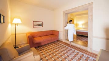A hotel room with a checkered floor, a sofa, a lamp, and a bed with a nightstand.