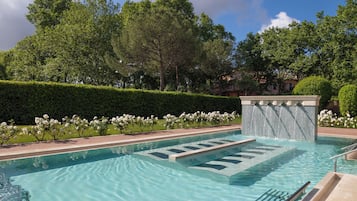 Piscina con agua cristalina, rodeada de follaje y un seto.