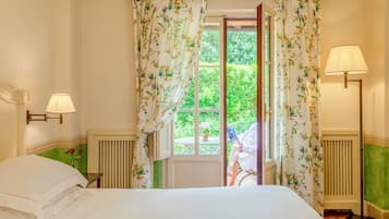 Ein Schlafzimmer mit einem Bett, zwei Nachttischlampen, einem Fenster mit Vorhängen und Blick auf Grünflächen.