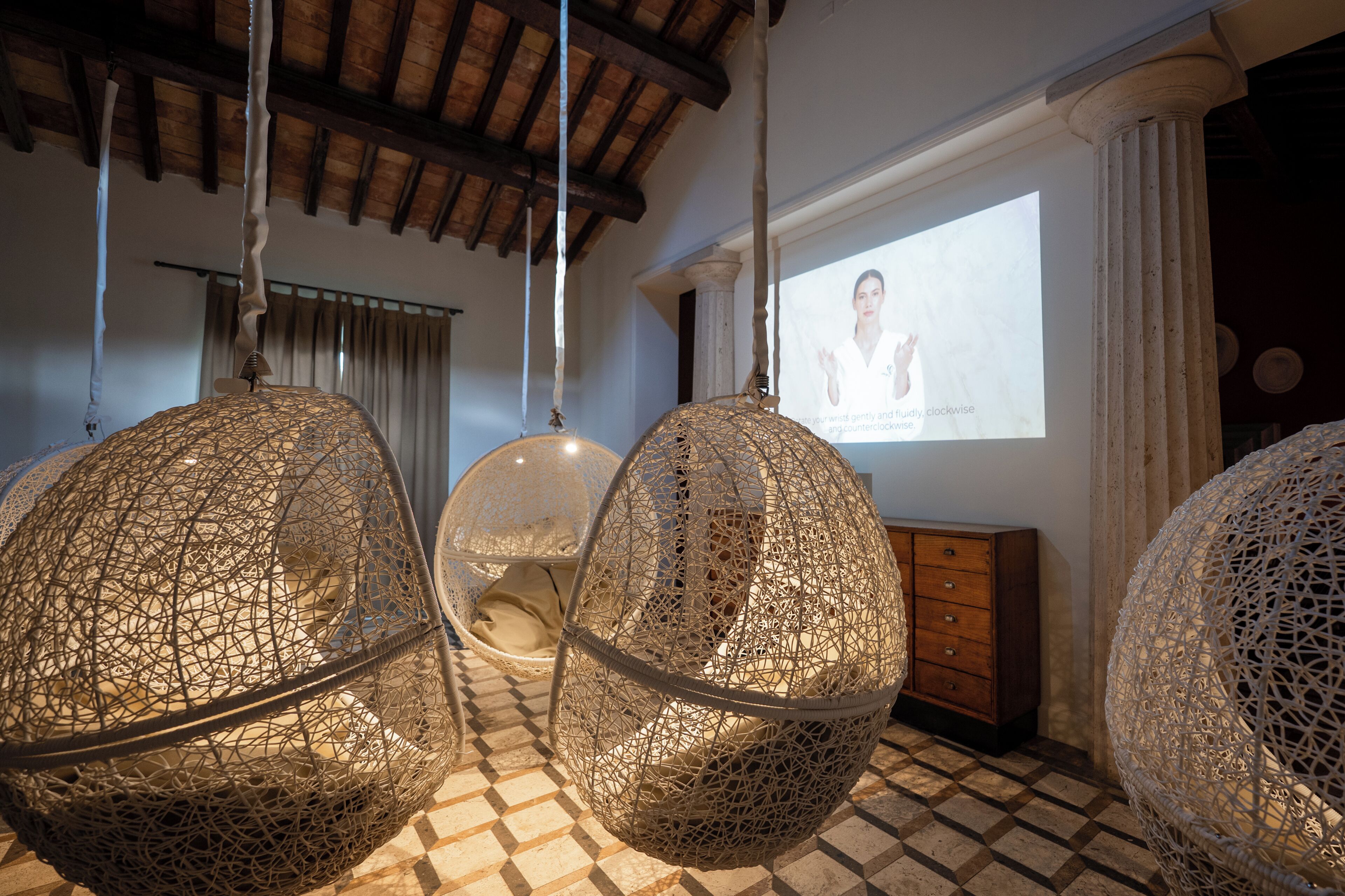 A room with hanging woven chairs, a projection screen, and a wooden cabinet.