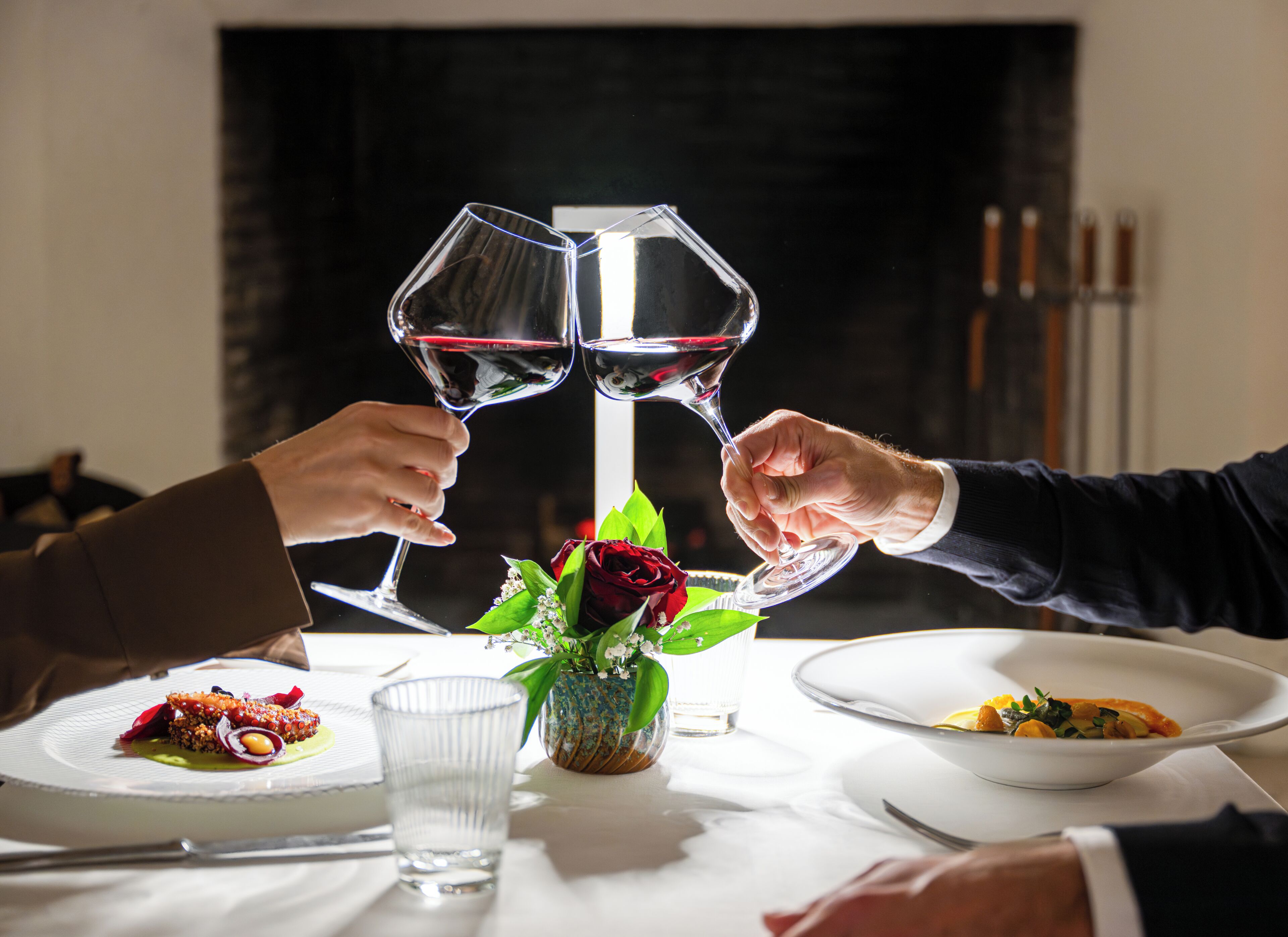 Una mesa de comedor con un vaso de agua, un florero con flores y platos de comida.