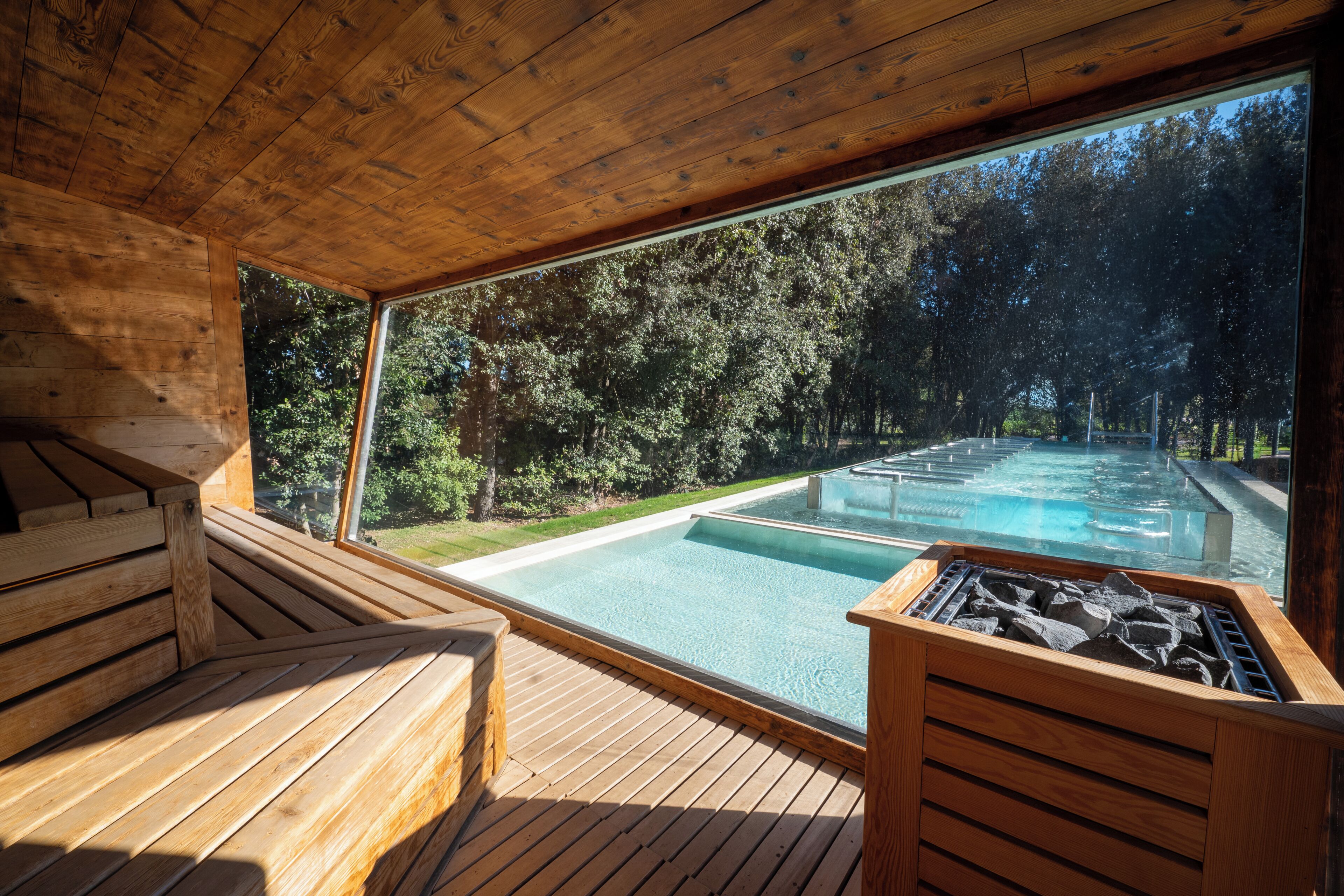 A wooden deck with a hot tub and a view of a pool and forest.