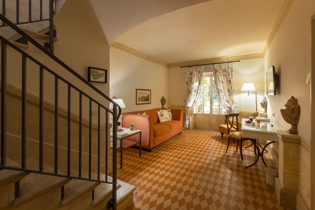 A living room with a checkered floor, a staircase, a sofa, a table, and a window with curtains.