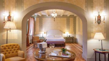 A hotel room with a bed, a round table with breakfast items, a chair, and two lamps.