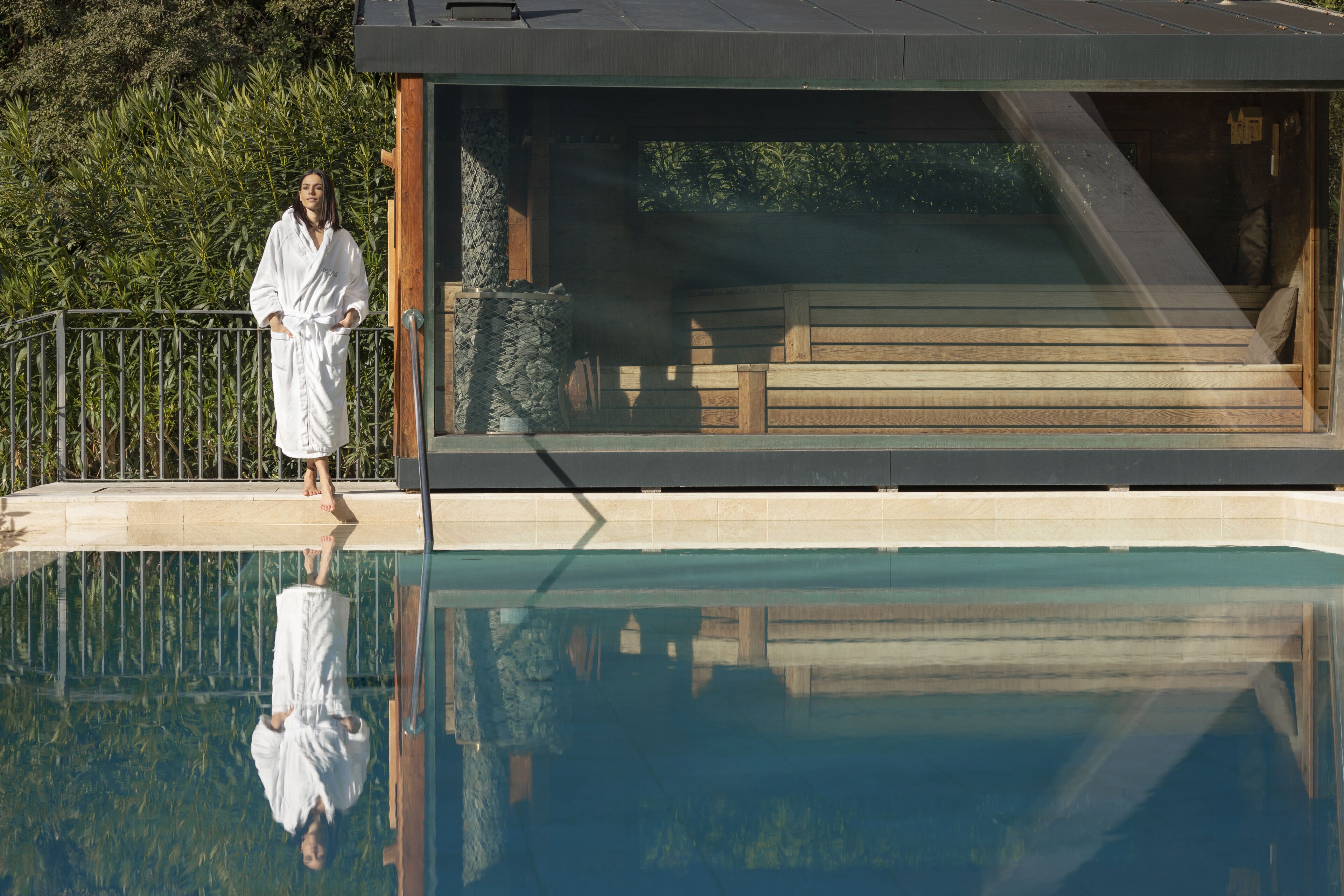 A modern building with a pool, wooden deck, and stone wall.