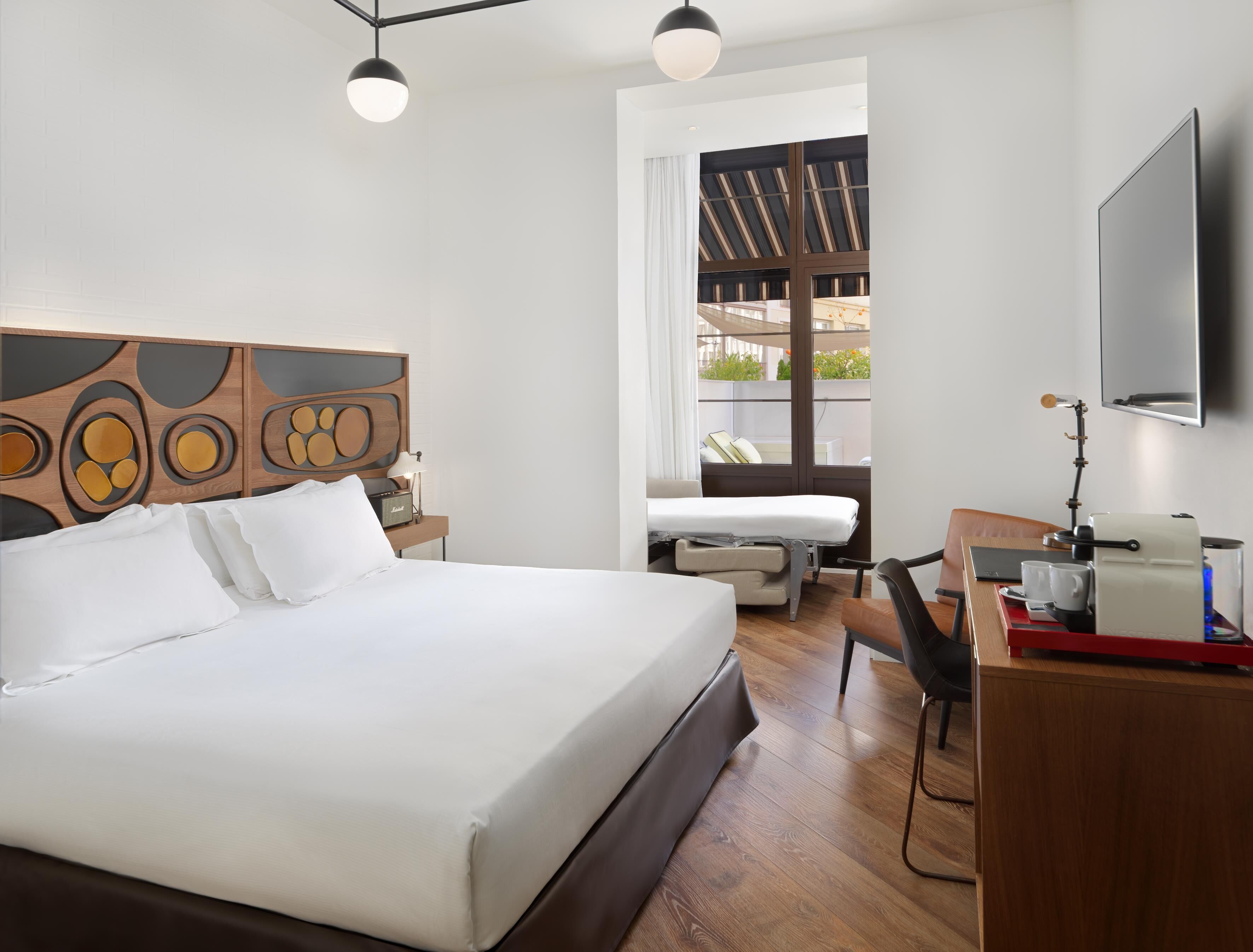 Una habitación de hotel moderna con una cama grande, un escritorio con silla, un televisor de pantalla plana y una ventana con vistas al exterior.