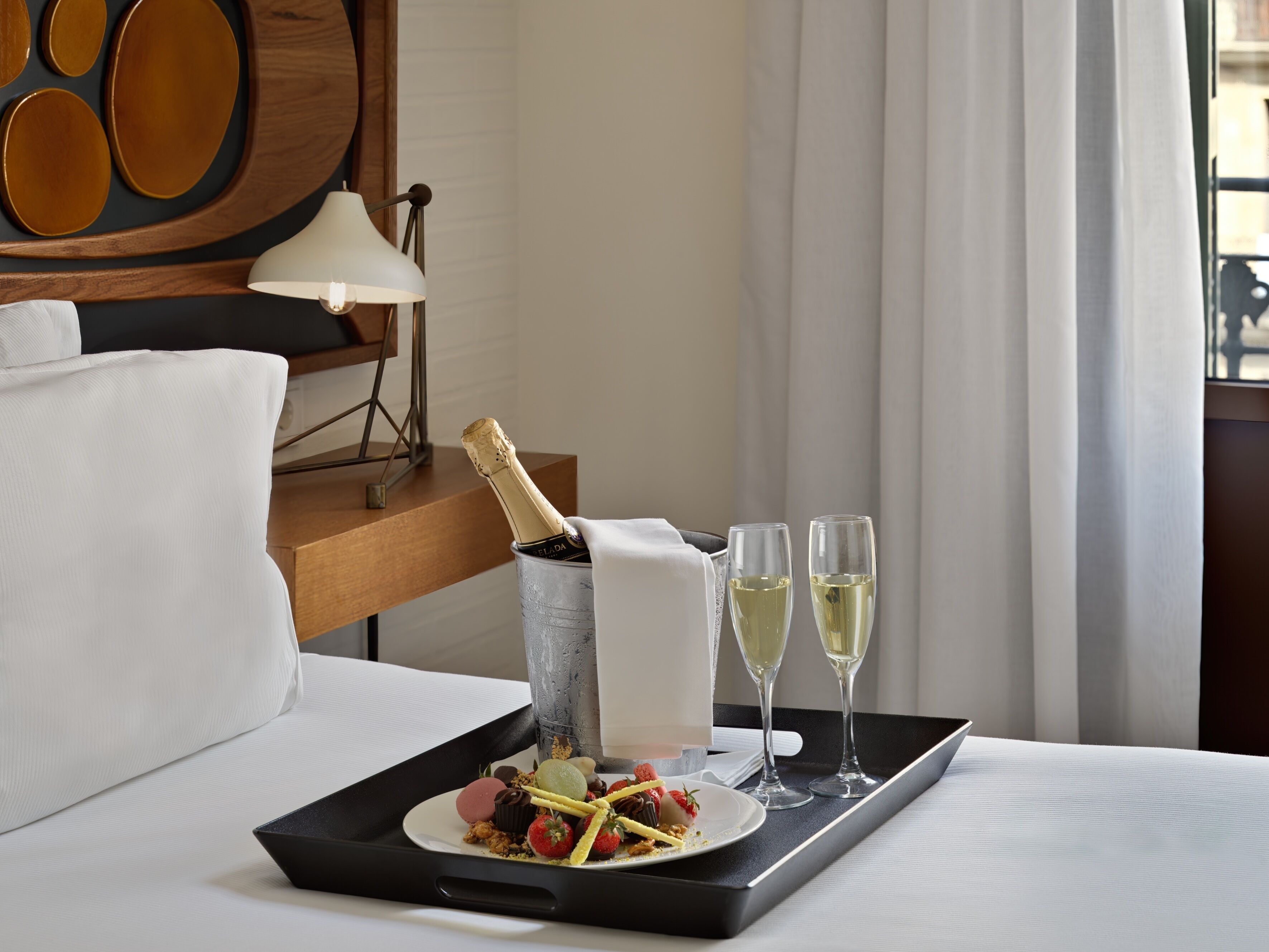 Un plateau avec une bouteille de champagne, deux coupes de champagne et une assiette de dessert posée sur un lit.