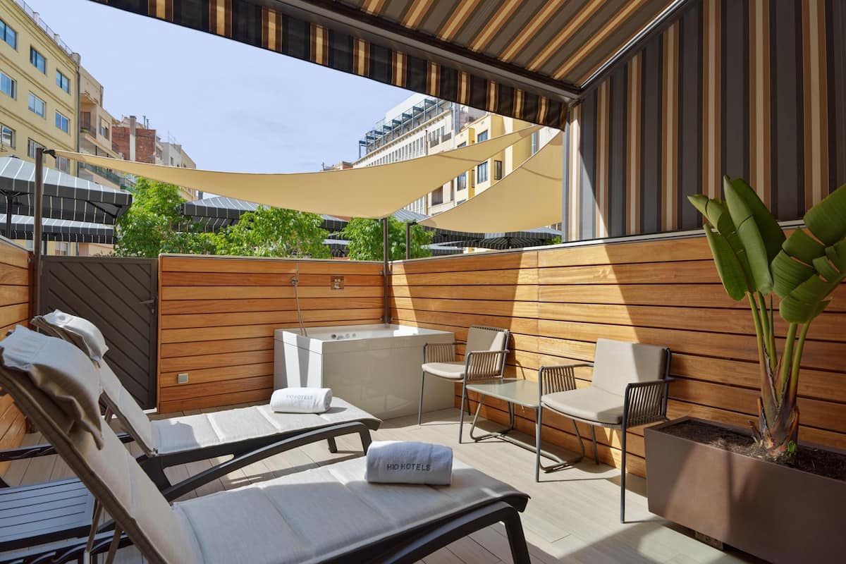 A rooftop terrace with lounge chairs, a table, and a potted plant.