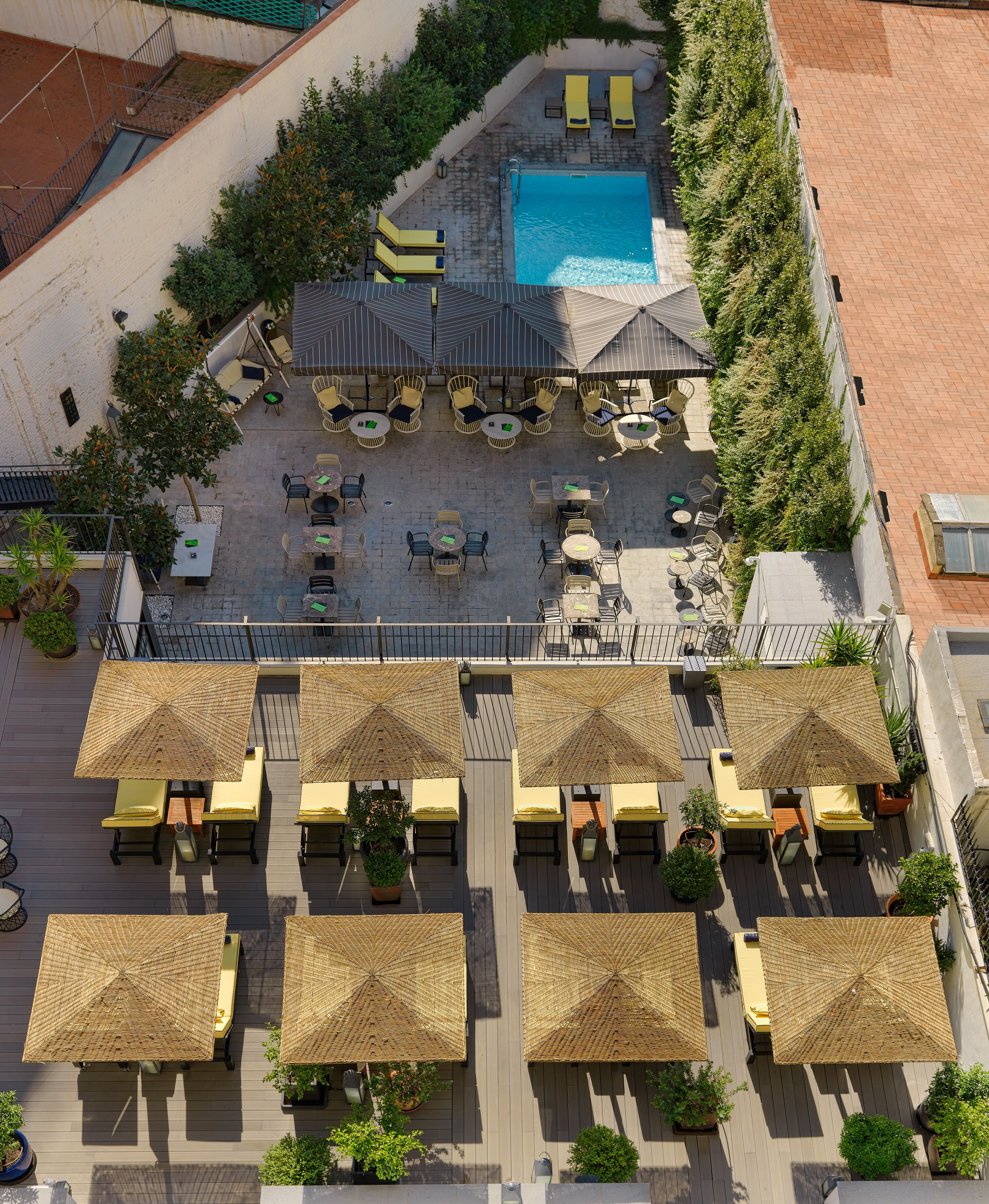 Vista aérea de un área de piscina en la azotea con sillones de descanso, sombrillas y una piscina.