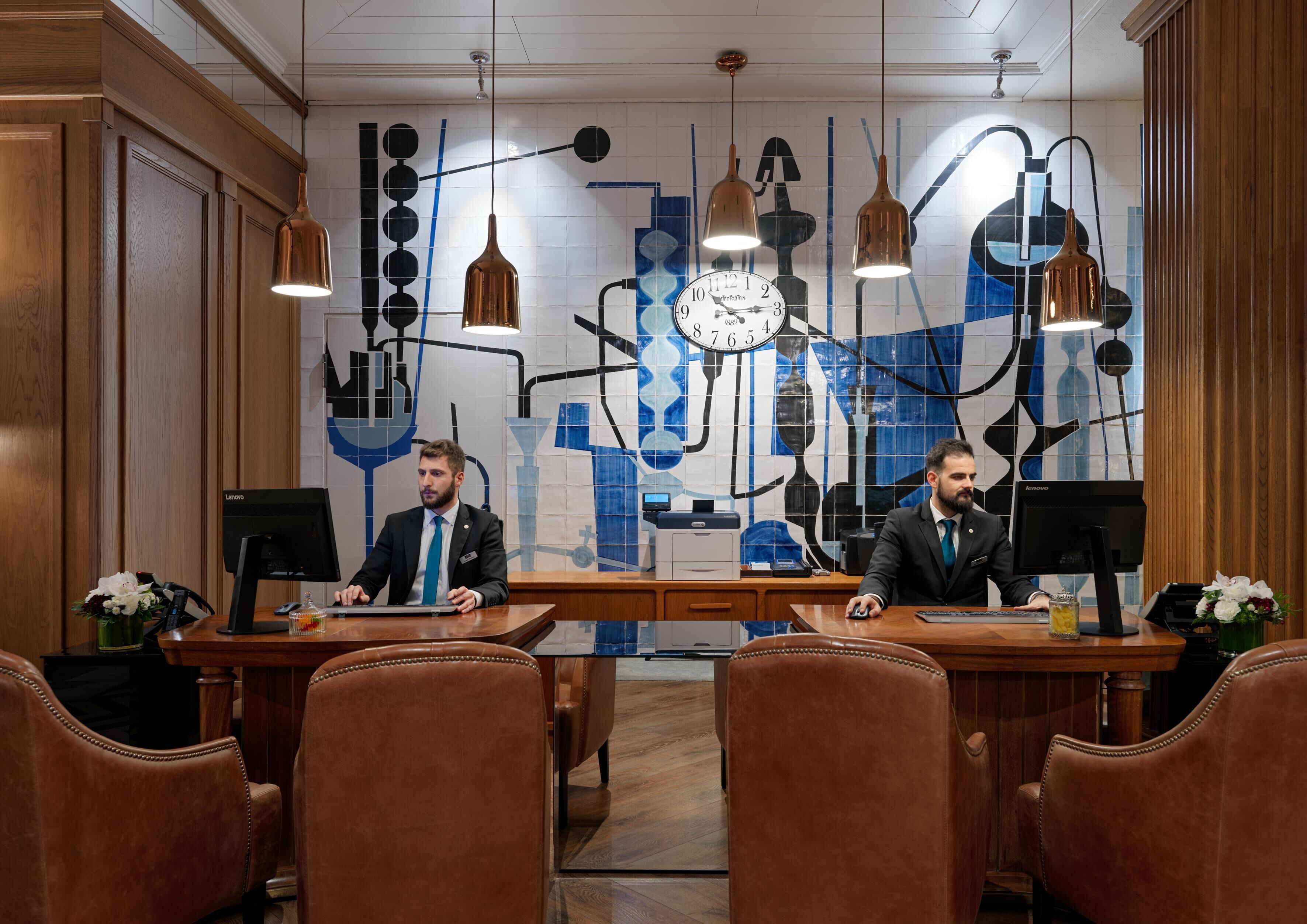 A conference room with two desks, leather chairs, and a wall with a clock and abstract art.