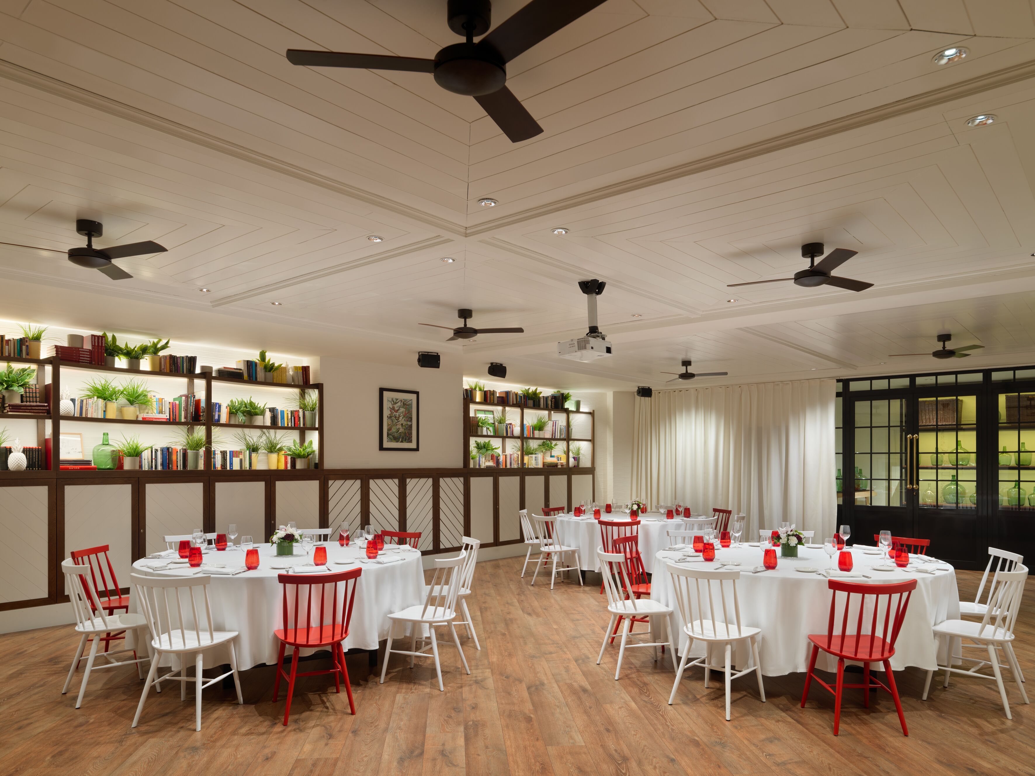 Un comedor amplio con mesas redondas, sillas blancas y detalles en rojo.