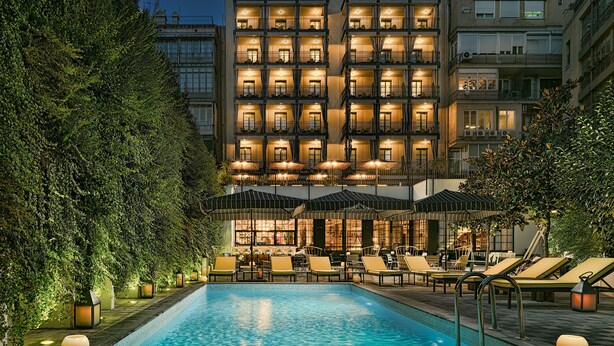 Un hotel con zona de piscina, mobiliario exterior y fachada iluminada.