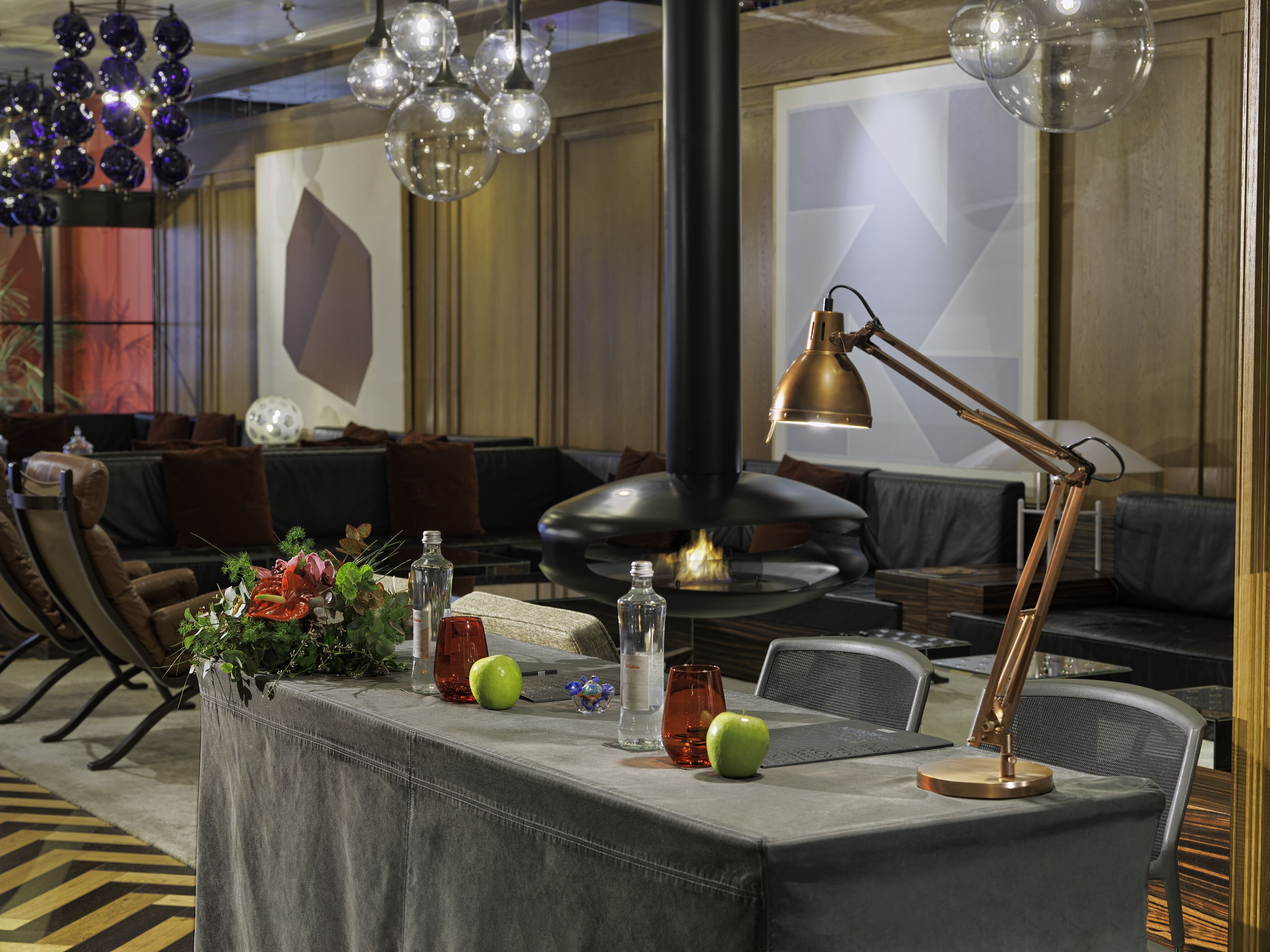 Un espacio lounge moderno con un sofá, una mesa con lámpara, botellas decorativas y una manzana verde.