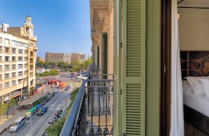 A hotel room with a balcony overlooking a busy street with cars and buses, and a view of historic buildings. - H10 Metropolitan (Barcelona)