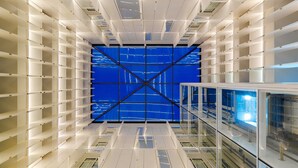 Un interior moderno con un diseño geométrico en el techo, superficies reflectantes y una estructura azul central.