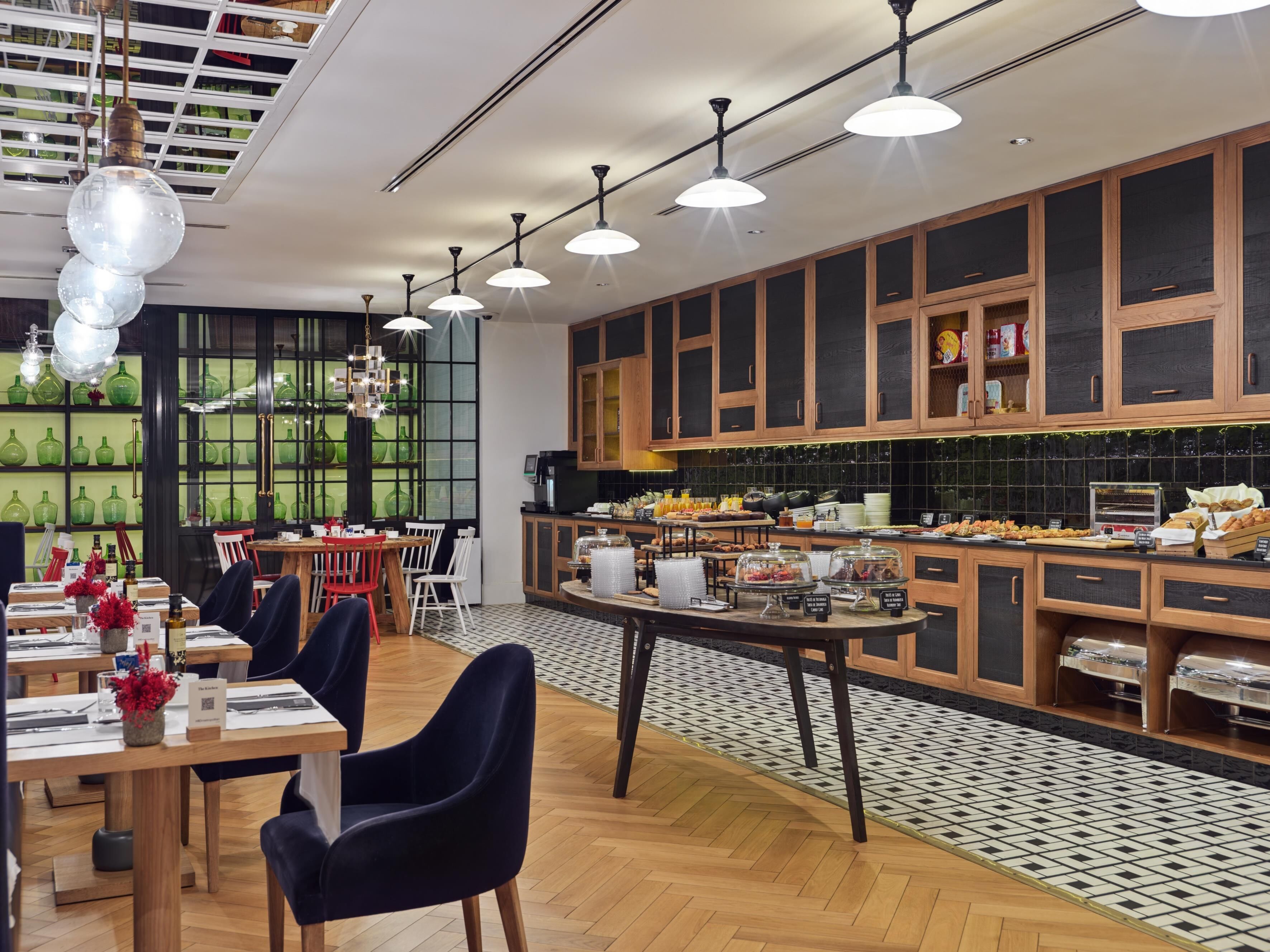 A modern restaurant with a central dining area, a buffet counter, and a kitchen visible through a glass partition.