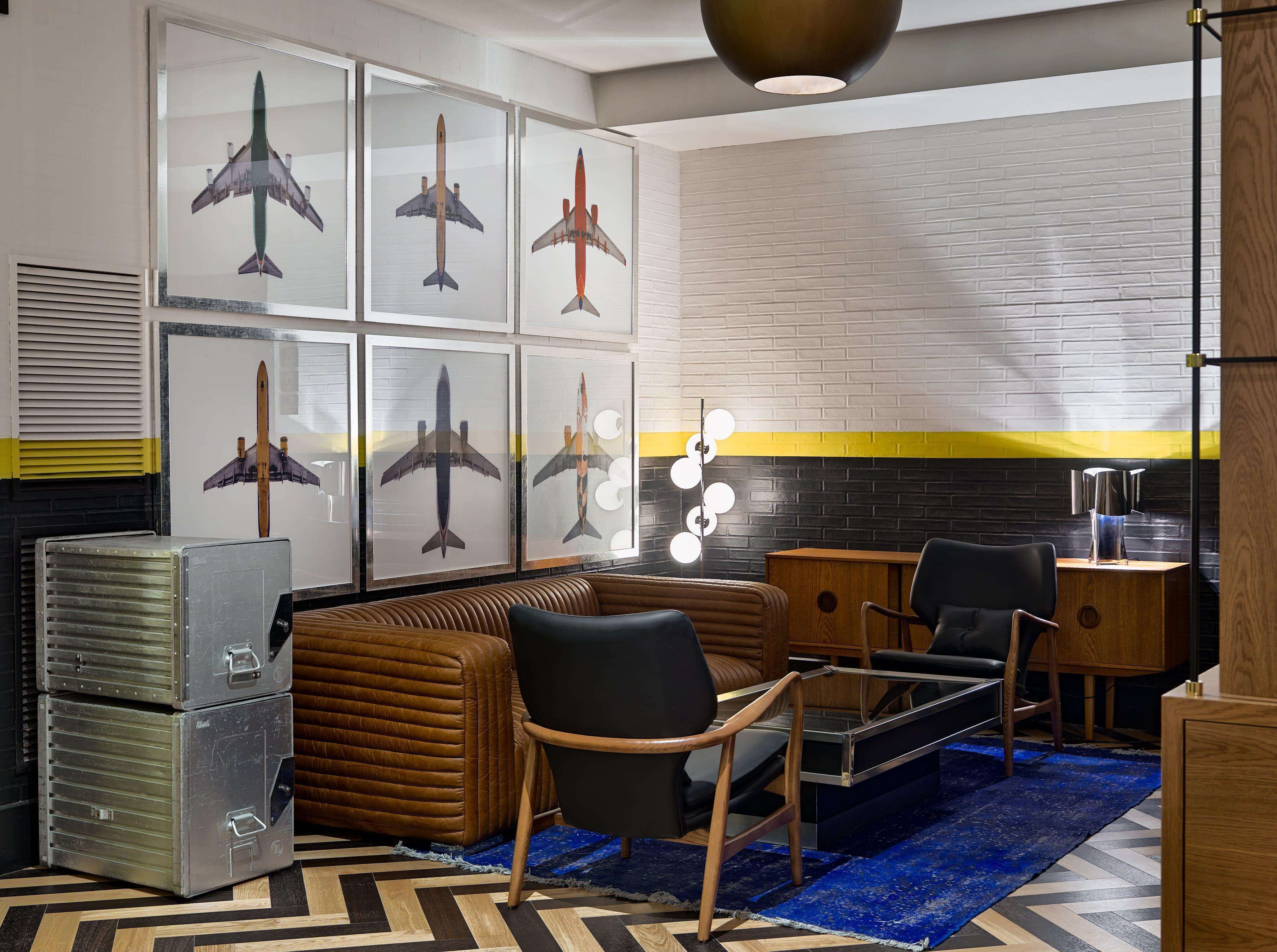 A modern lounge with a brick wall, a blue rug, and framed airplane pictures.