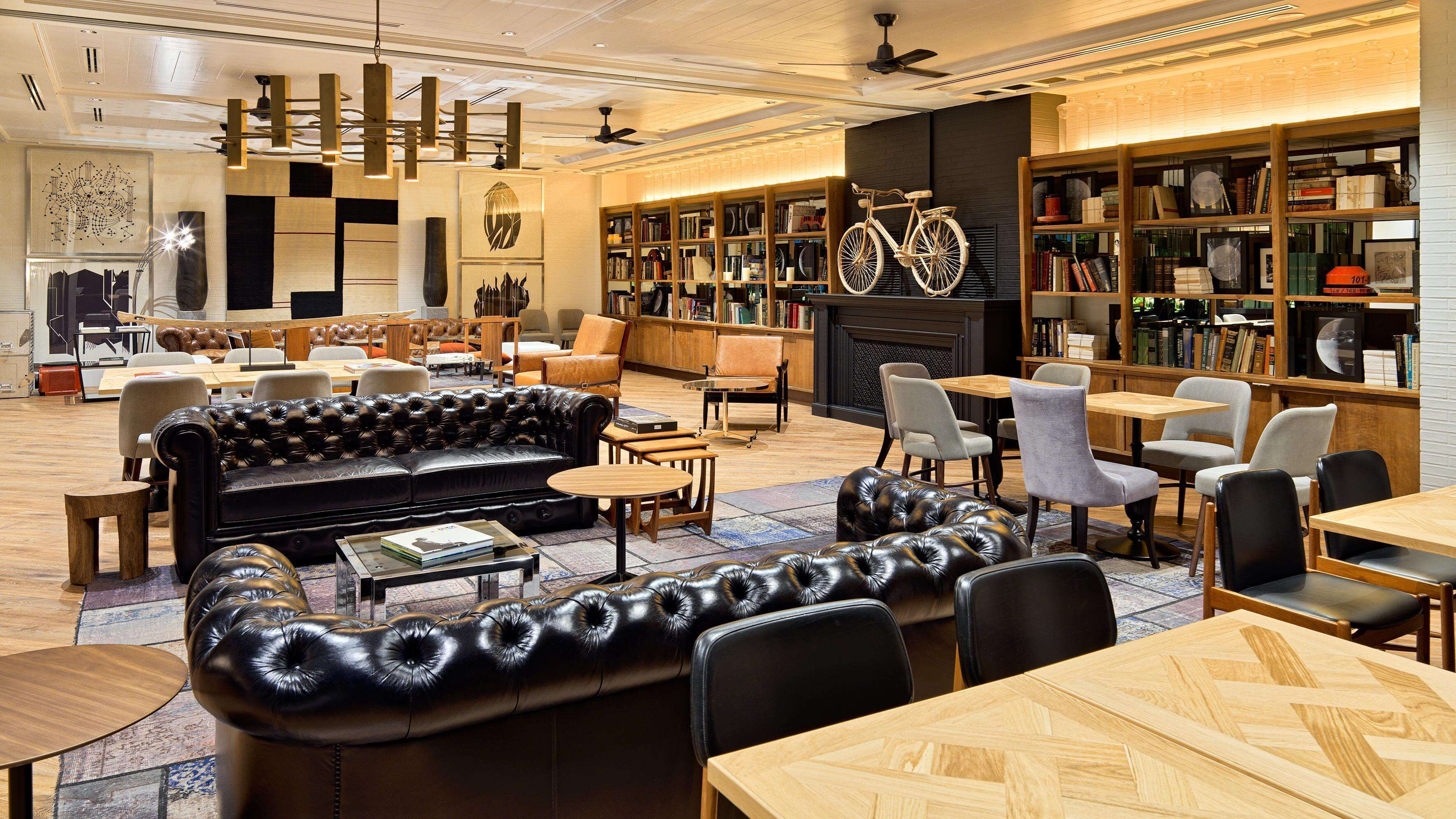 A modern library with leather sofas, wooden tables, and bookshelves filled with books.