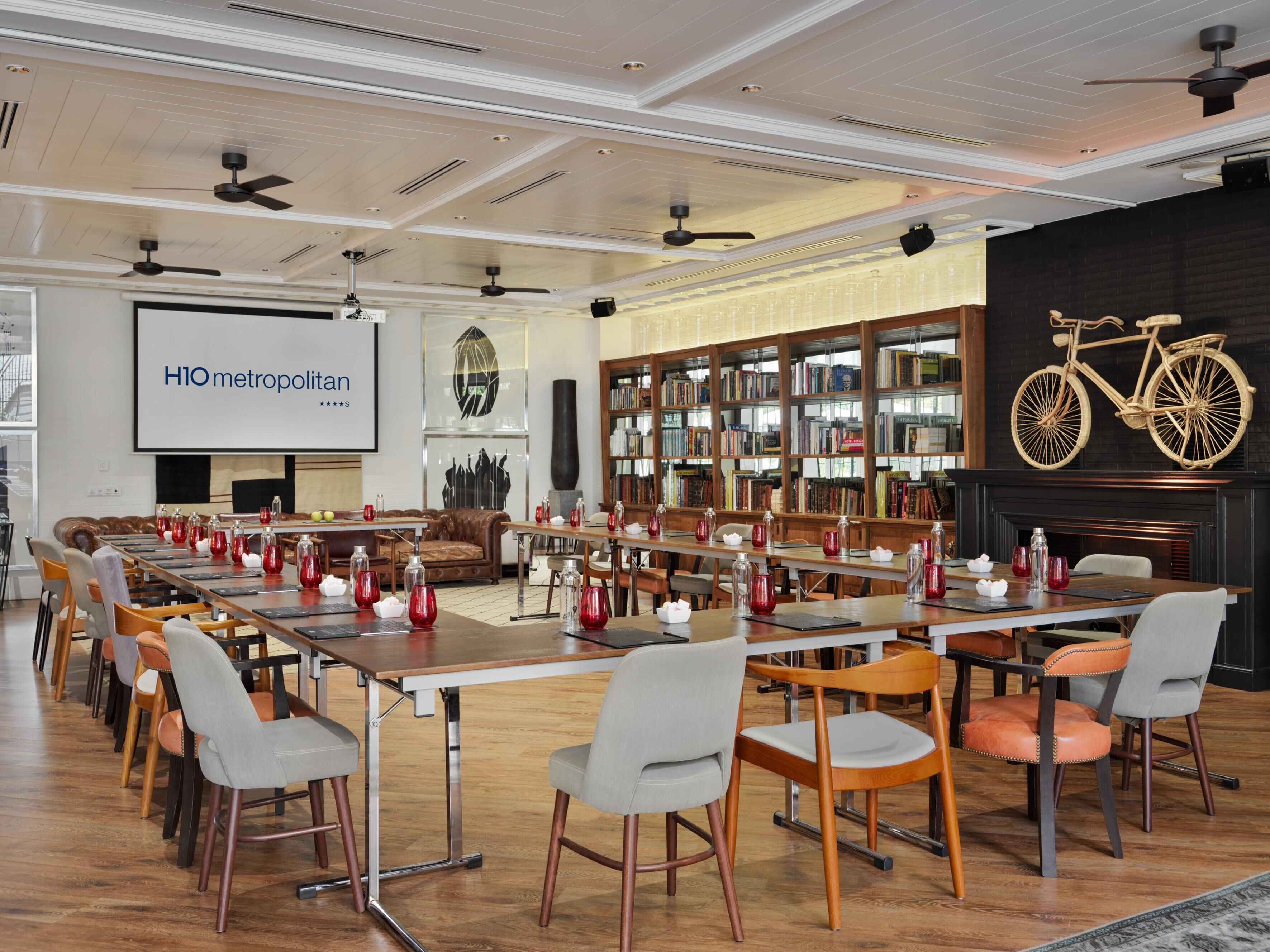 A conference room with a long table, chairs, a projector screen, and a bookshelf.