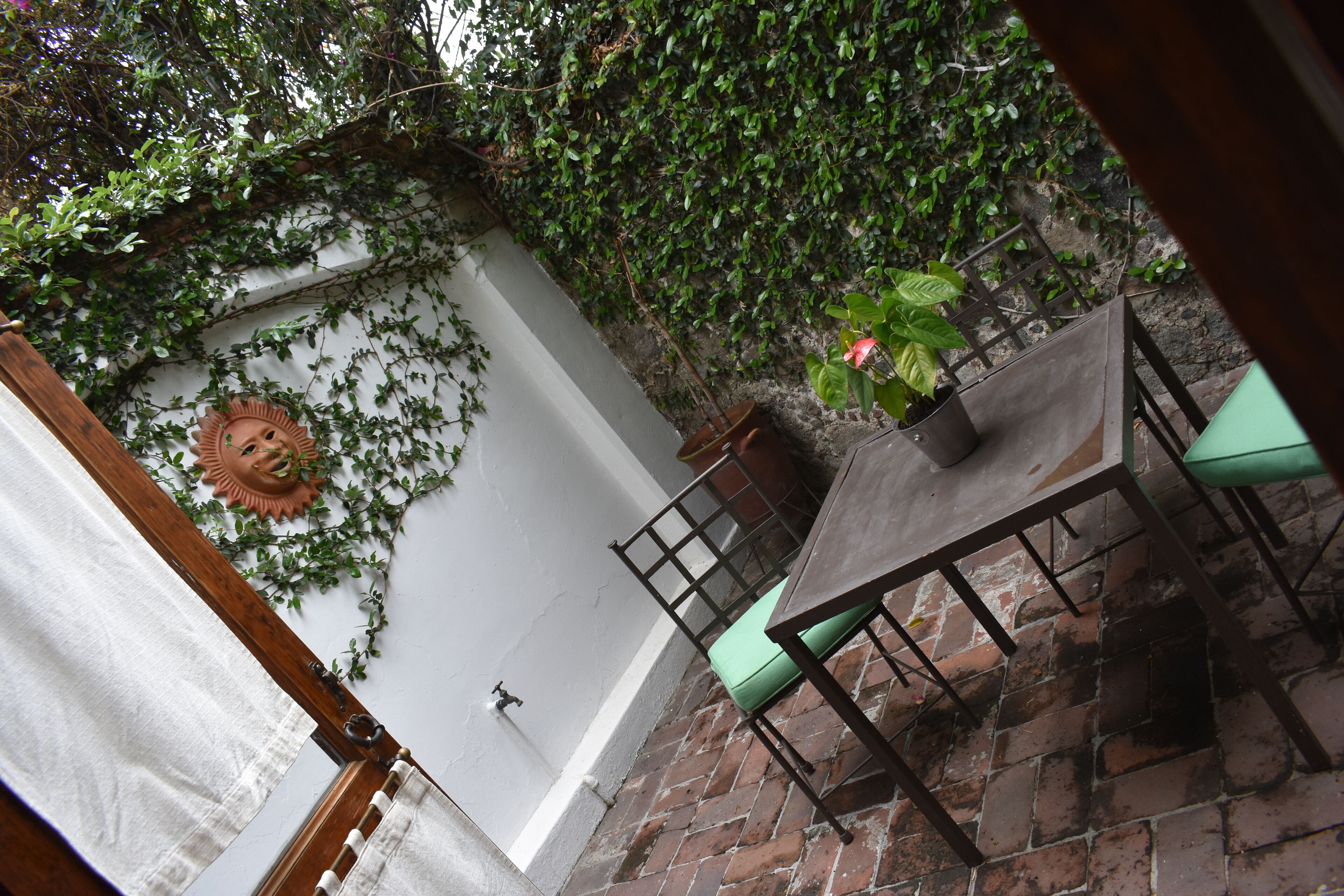 Un patio con piso de ladrillo, una mesa con sillas y una planta en maceta.