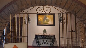 A room with a white cushioned chair, a small table with a plant, and a painting on the wall. - Hotel Boutique La Joyita (Cuernavaca)