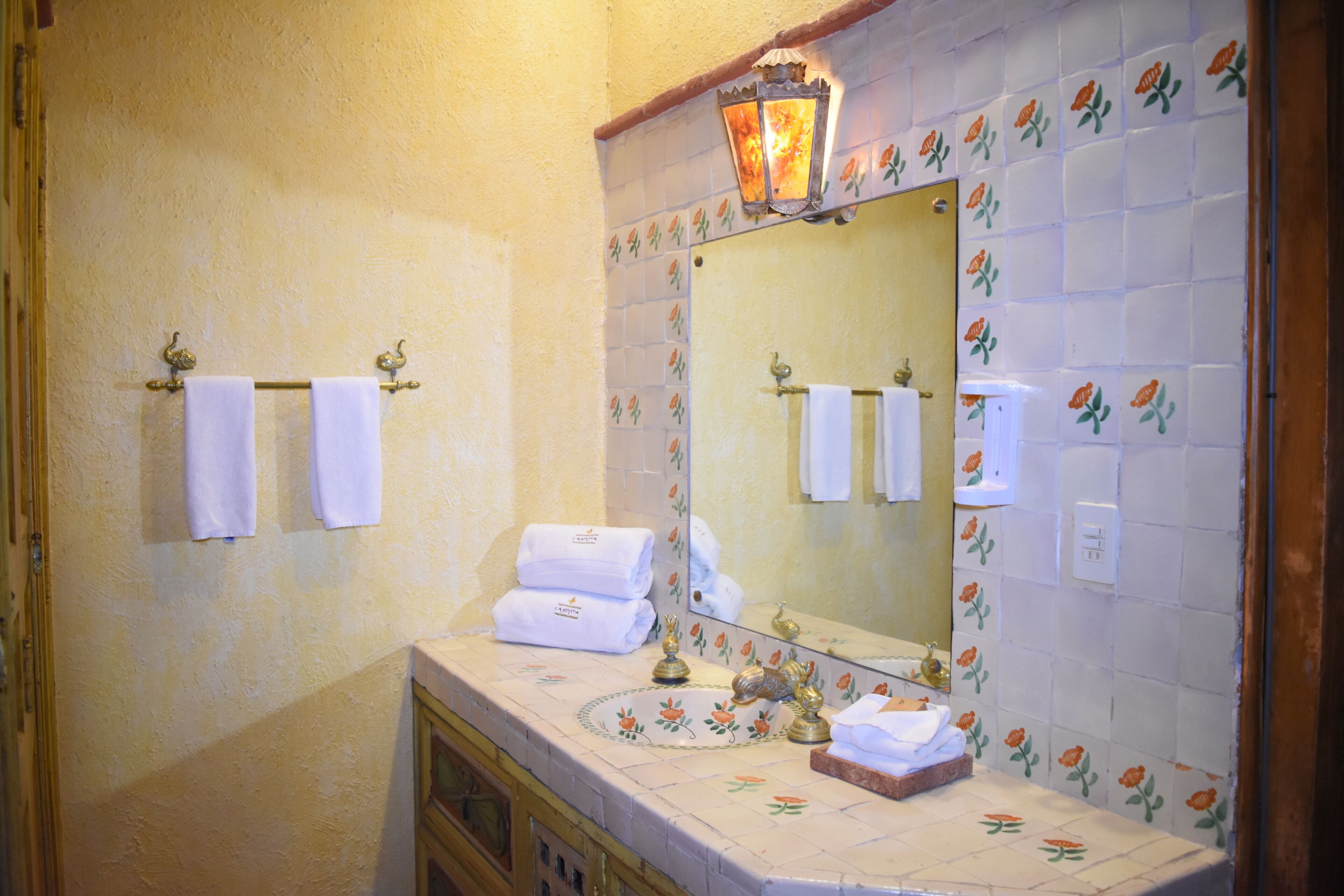 Een badkamer met een betegelde muur, een wastafel met spiegel en twee handdoeken aan haken.