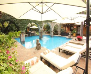 Una piscina al aire libre, sombrillas, sillones reclinables de piscina