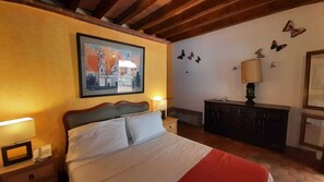 Quarto de hotel com cama, abajures, um quadro, cômoda e decorações nas paredes.