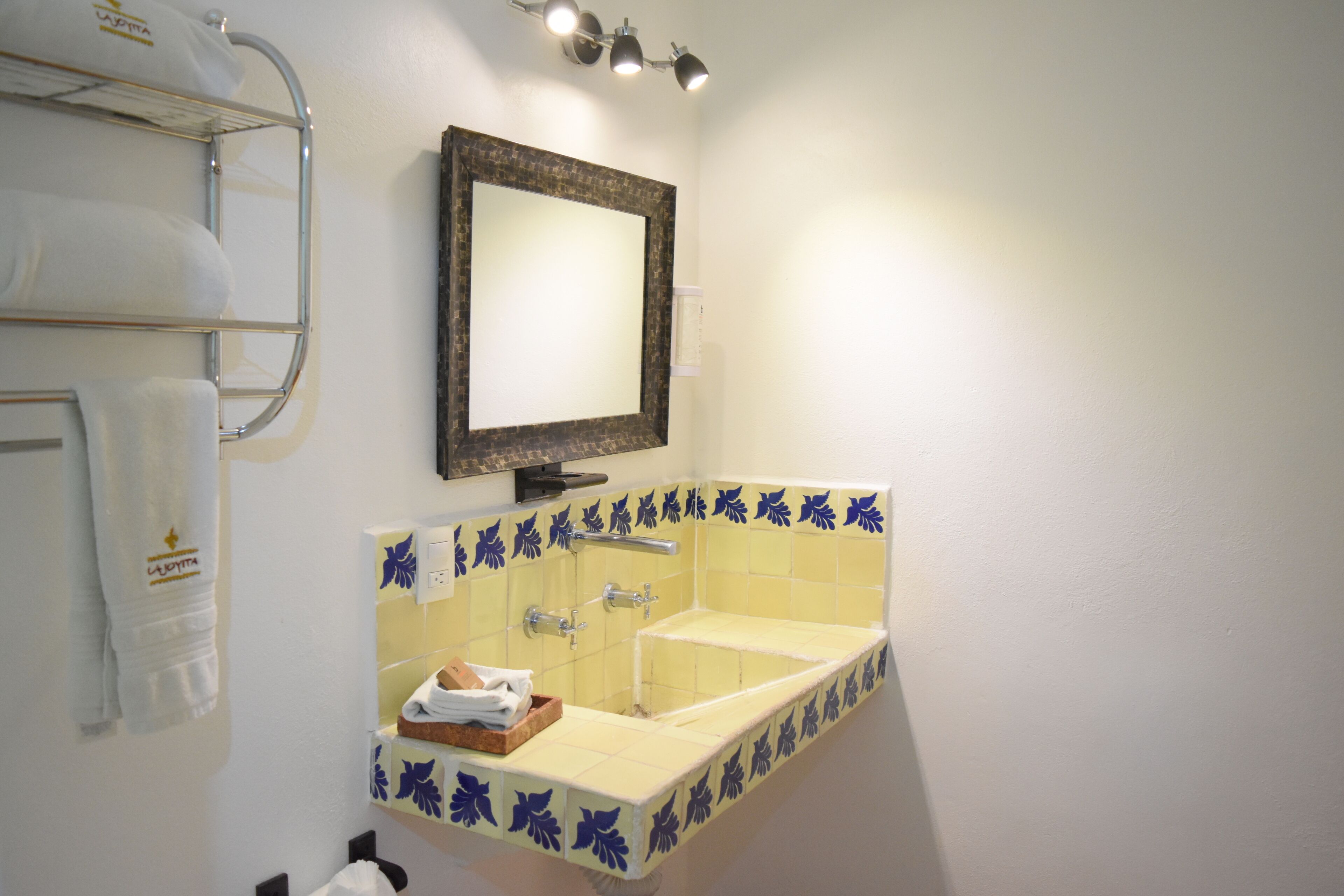 A bathroom with a sink, mirror, towel rack, and a shelf with towels.