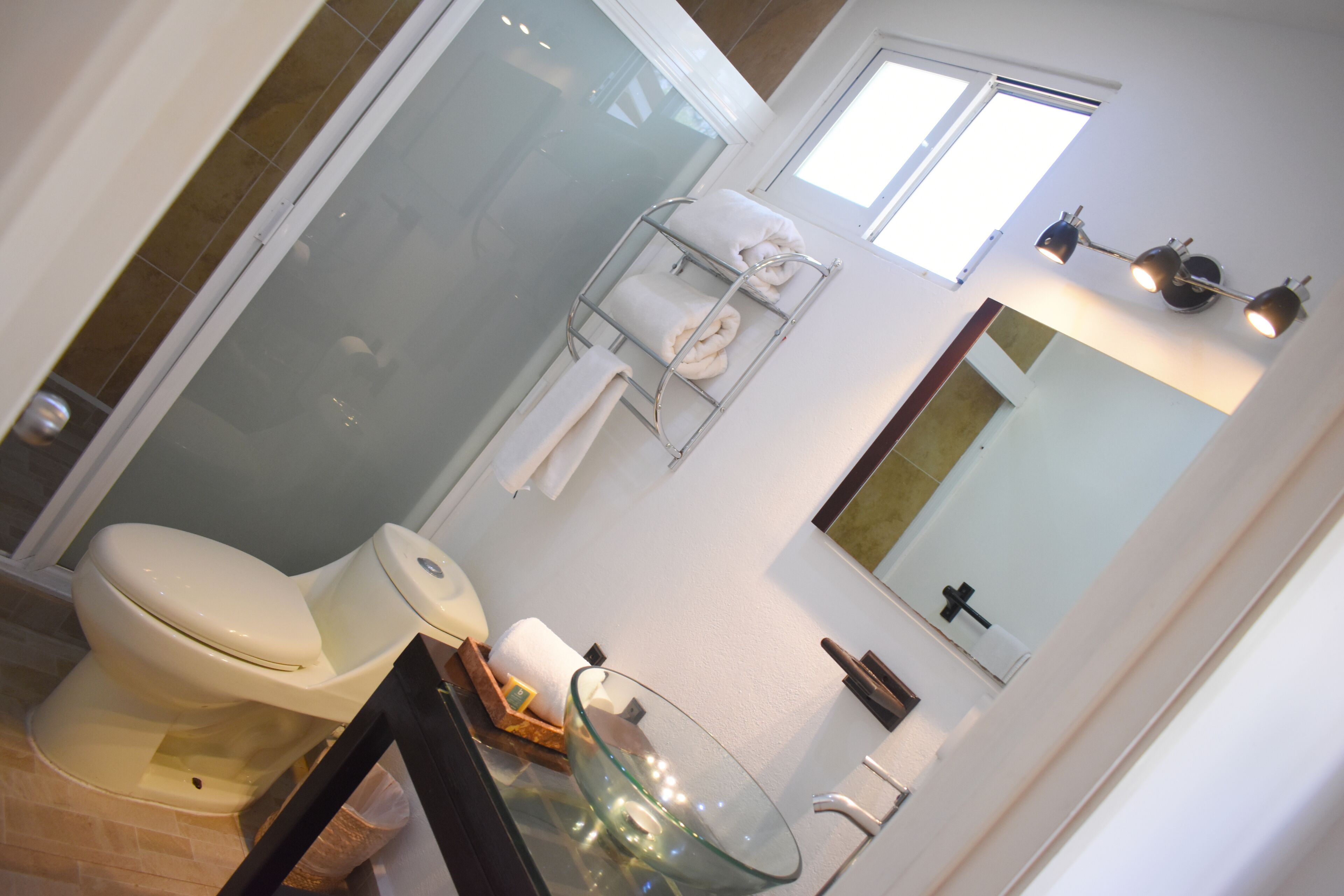 Ein modernes Badezimmer mit einer Duschkabine aus Glas, einer Toilette, einem Waschbecken aus Glas und einem Handtuchhalter mit einem weißen Handtuch.